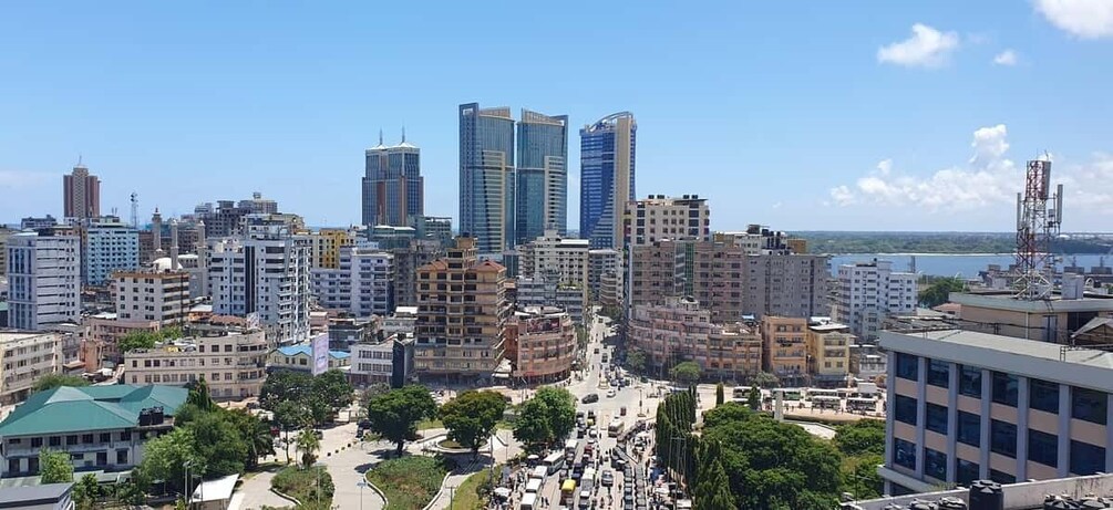 A cityscape with modern high-rise buildings, a busy street, and a body of water in the background. 3