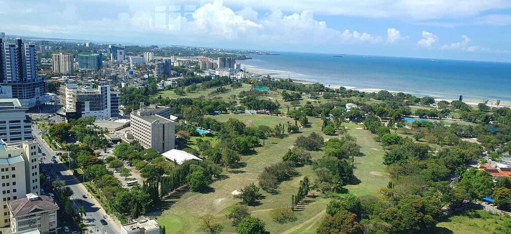 A coastal cityscape with a park, buildings, and a beach. 2