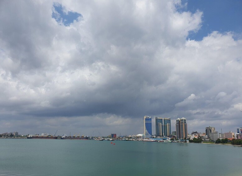 A coastal cityscape with a large body of water, several high-rise buildings, and a cloudy sky. 1
