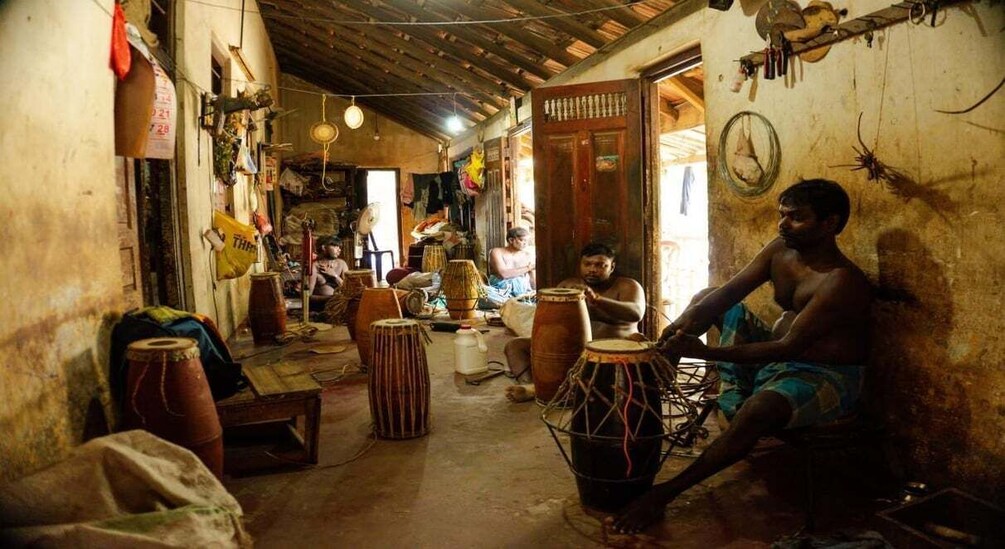 A rustic interior with traditional drums, wooden furniture, and a person playing a drum. 3