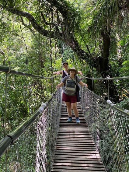 Two people walking on a wooden suspension bridge surrounded by dense greenery. 5