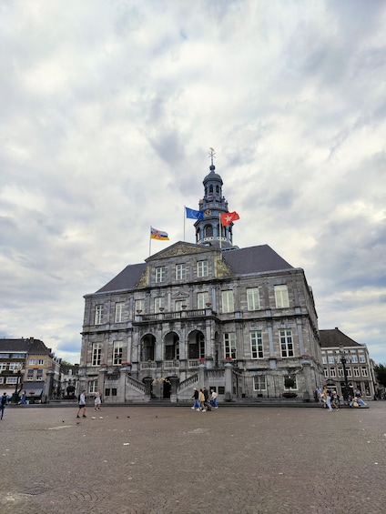 A historic building with a clock tower, flags, and a cobblestone plaza. 4