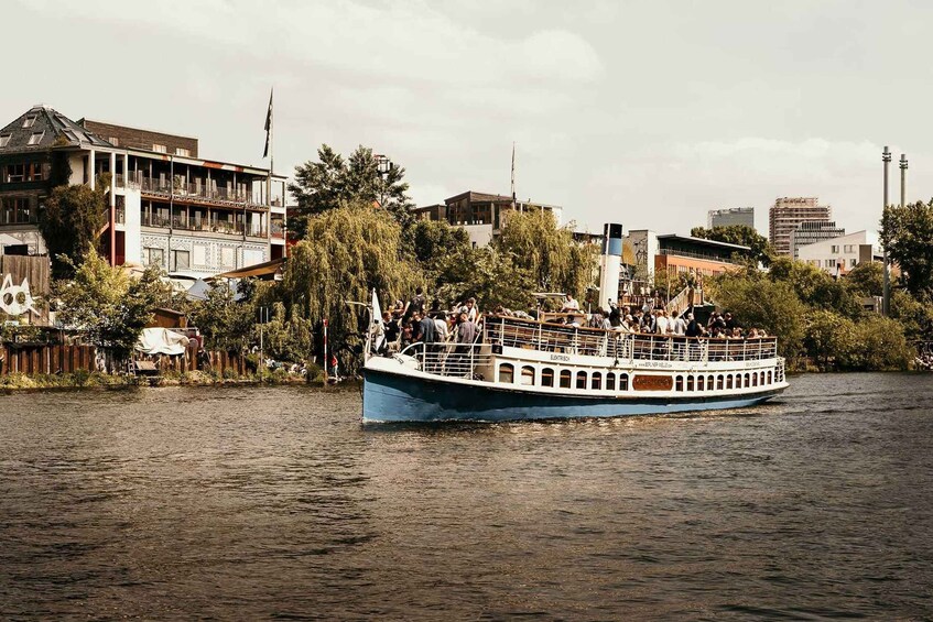 A boat with passengers on a river, surrounded by buildings and trees. 3