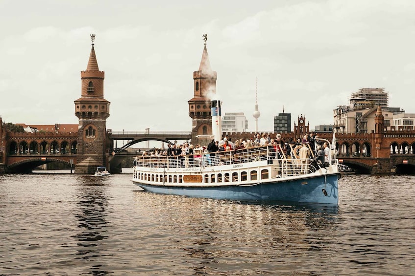 A boat with passengers on a river, a bridge, and historic towers in the background. 1