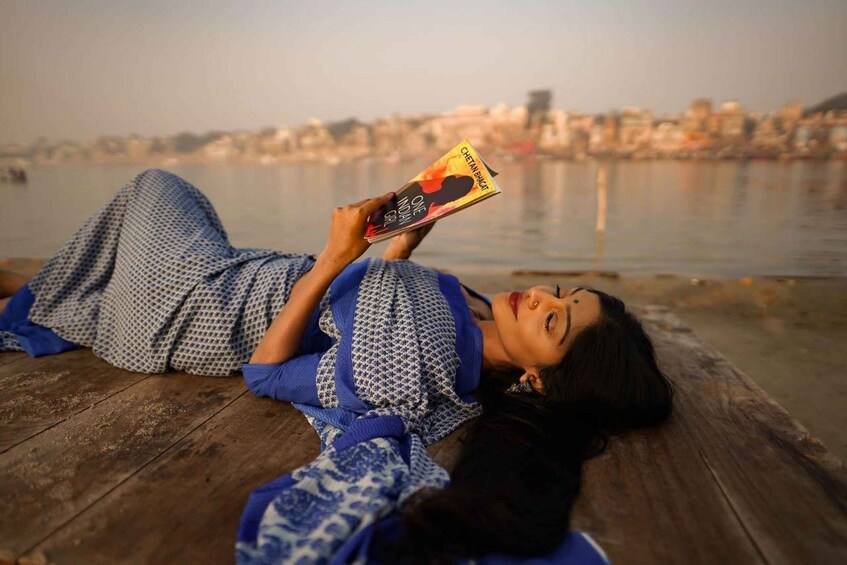 Una persona recostada sobre un muelle de madera, leyendo un libro titulado 'One Indian Girl'. 1