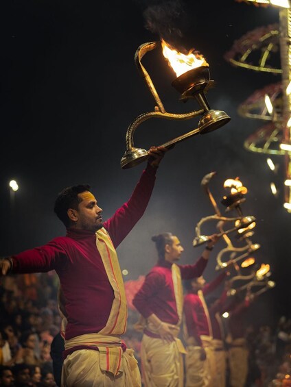 Una persona sosteniendo una antorcha encendida, rodeada de otras personas con atuendo similar, probablemente participando en un evento ceremonial. 3
