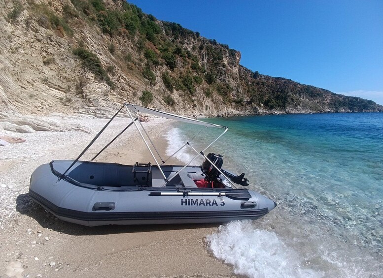 Ein Boot namens 'HIMARA 3' an einem Strand mit klarem Wasser und felsigen Klippen im Hintergrund. 5