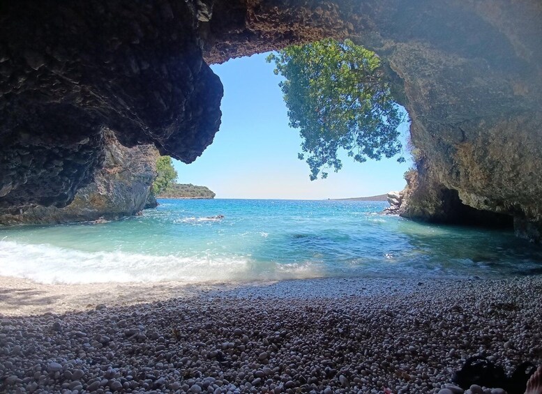 Ein felsiger Strand mit klarem türkisblauem Wasser, einem Höhleneingang und einem Baum darüber. 3