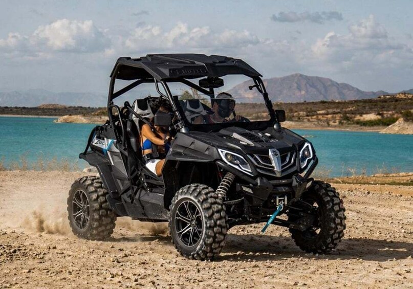 A black off-road vehicle on a dirt path near a body of water with mountains in the background. 1