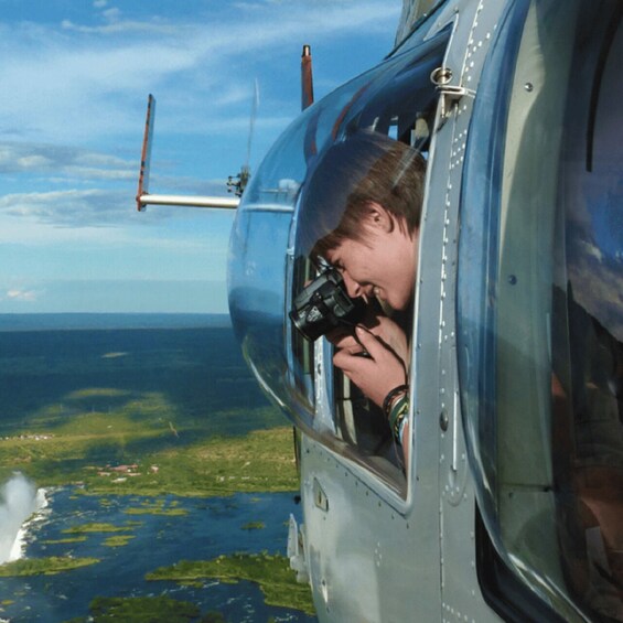 A person inside a helicopter taking a photograph of a coastal landscape with water and greenery. 1