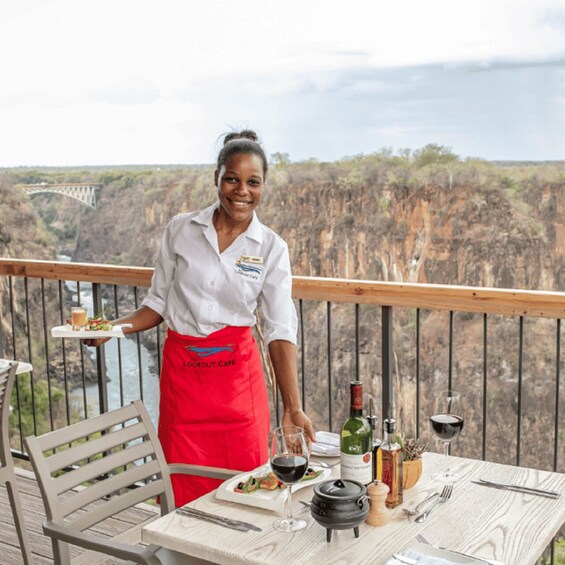A person serving food on a balcony with a scenic cliff view. 5