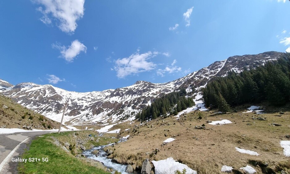 A mountainous landscape with a road, snow patches, and evergreen trees. 2