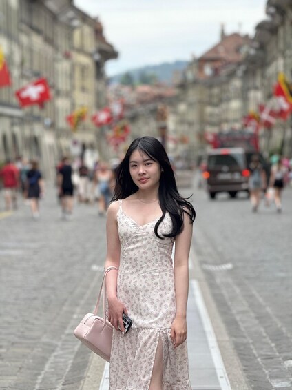 A person standing on a cobblestone street with buildings and flags in the background. 1