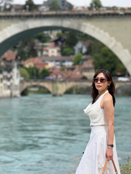 A woman in a white dress standing by a river with a stone bridge in the background. 4