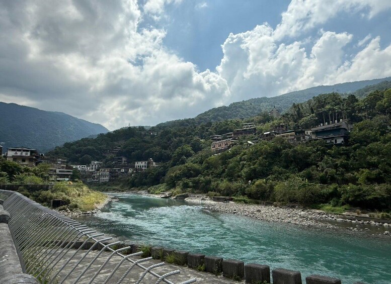 A river flowing through a mountainous area with houses on the hillside and a bridge in the foreground. 3