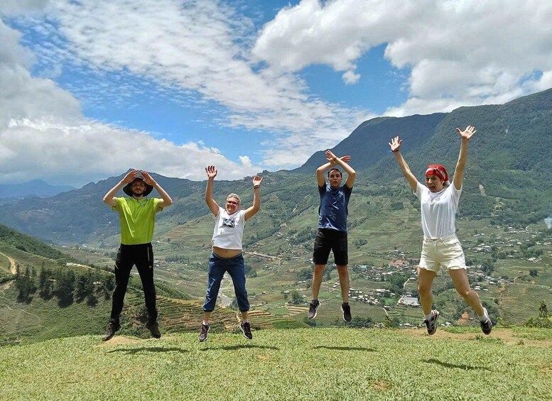 Four people jumping on a grassy hill with a mountainous landscape in the background. 1