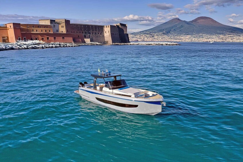 A boat on clear turquoise water with a coastal fort and a mountain in the background. 3