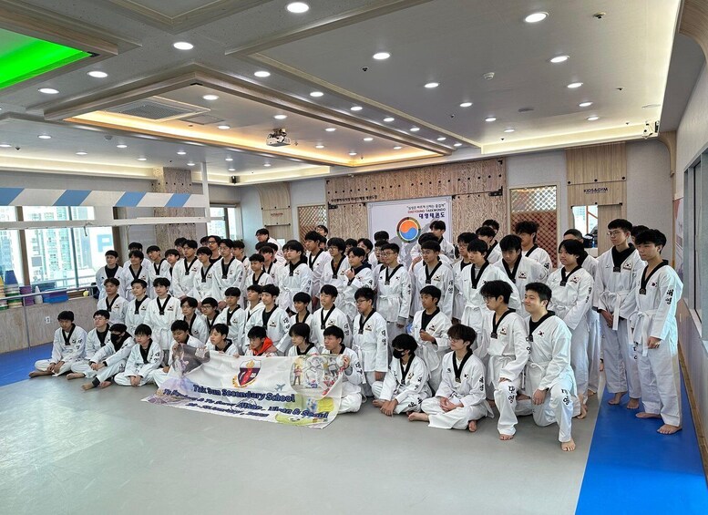 A group of people in white martial arts uniforms posing for a photo in a gymnasium with a banner in the background. 3