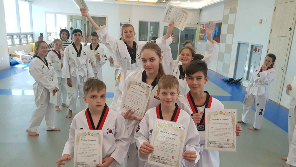 A group of individuals in a martial arts training facility, holding certificates of completion. 5