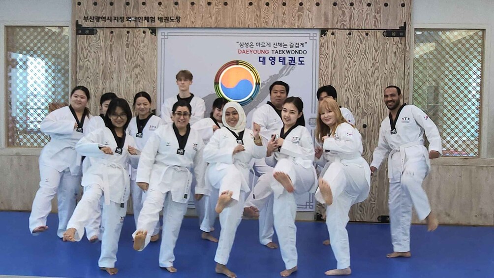 A group of people in white martial arts uniforms posing for a photo in a training hall with a banner in the background. 2