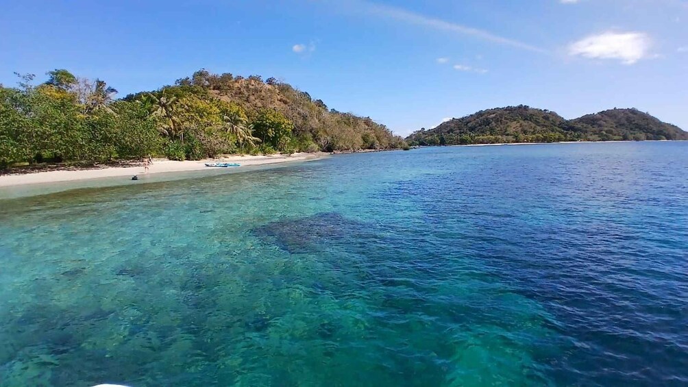 A clear tropical beach with turquoise water, a sandy shore, and lush green hills in the background. 2