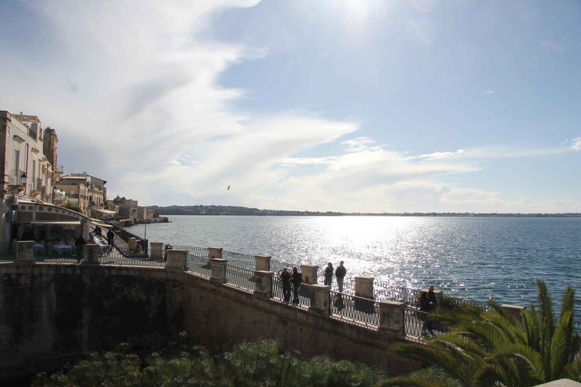 A waterfront promenade with people walking, overlooking a calm sea under a clear sky. 2