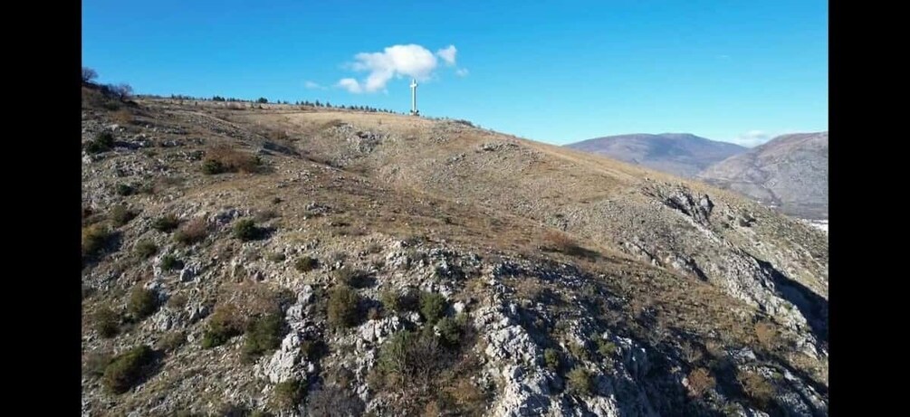 A rocky hillside with sparse vegetation and a cross on top. 5
