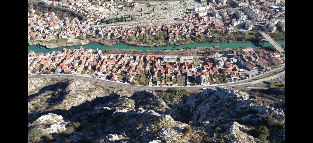 An aerial view of a town with a river, rocky terrain, and a mix of residential and commercial buildings. 1