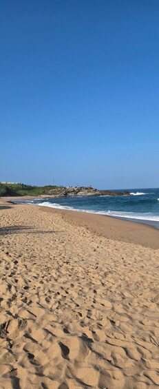 A sandy beach with gentle waves, a rocky outcrop, and a clear blue sky. 5