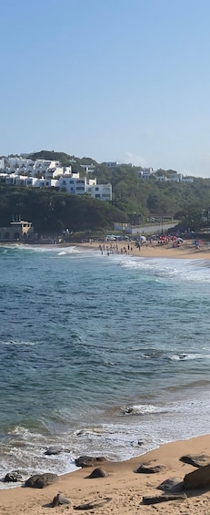 A beach with waves, people, and white buildings on a hillside. 4