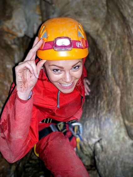 A person in a red climbing suit and yellow helmet, sitting in a cave. 5