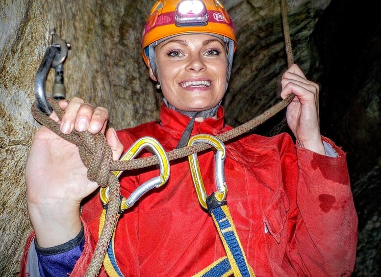 A person in a red jacket with a helmet and climbing gear, holding a rope and carabiner. 3