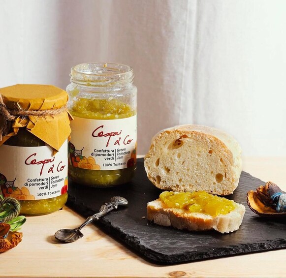 A jar of green tomato jam, a loaf of bread, and a slice of bread with jam on a slate board. 1