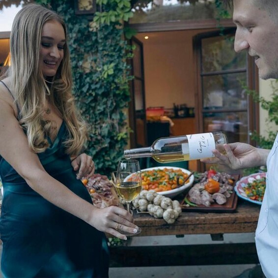 Two people toasting with wine glasses, a bottle of wine, and a table with various dishes and a bottle of champagne. 3