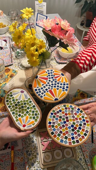 A table with mosaic coasters, a QR code, and yellow flowers. 4