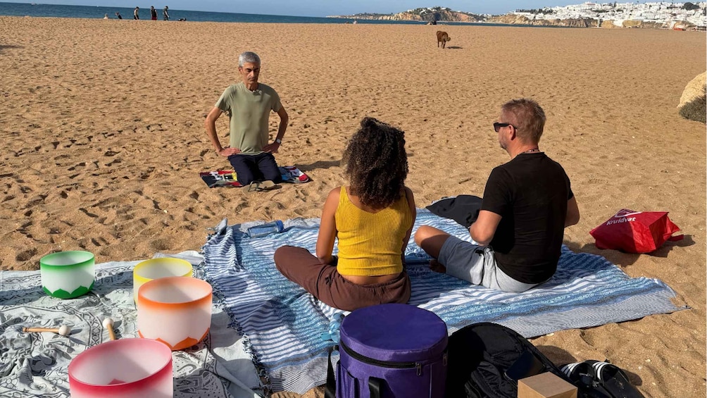 A beach scene with people sitting on a blanket, a dog in the background, and various items like bowls and a bag on the ground. 5