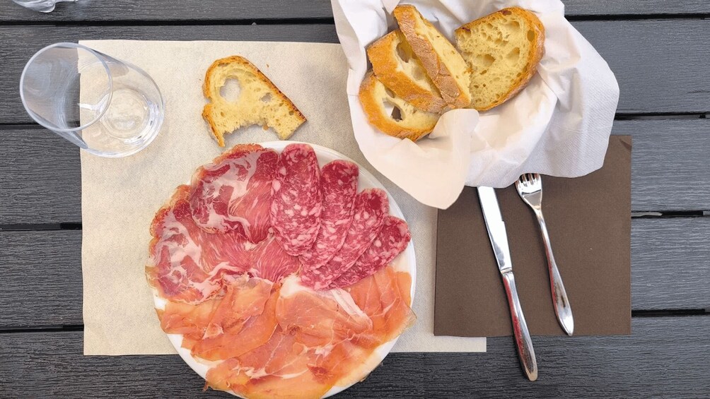 A plate of cured meat, a glass of water, and slices of bread on a wooden table. 2
