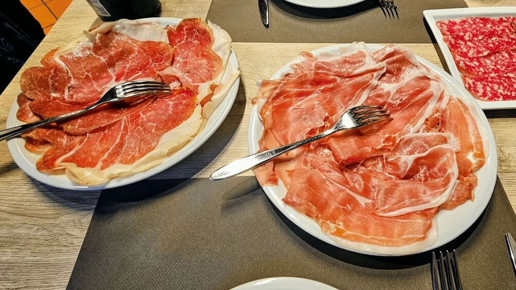 Two plates of sliced prosciutto on a wooden table. 5