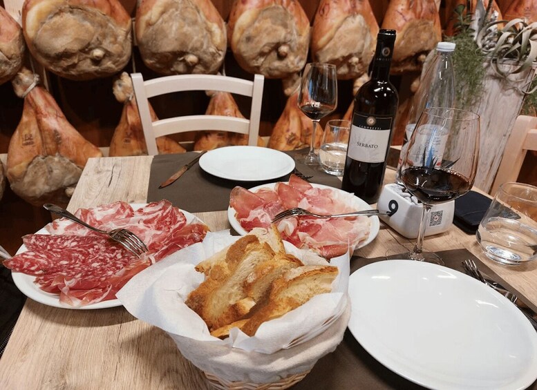A table set for a meal with plates of cured meats, a bottle of wine, and bread. 5