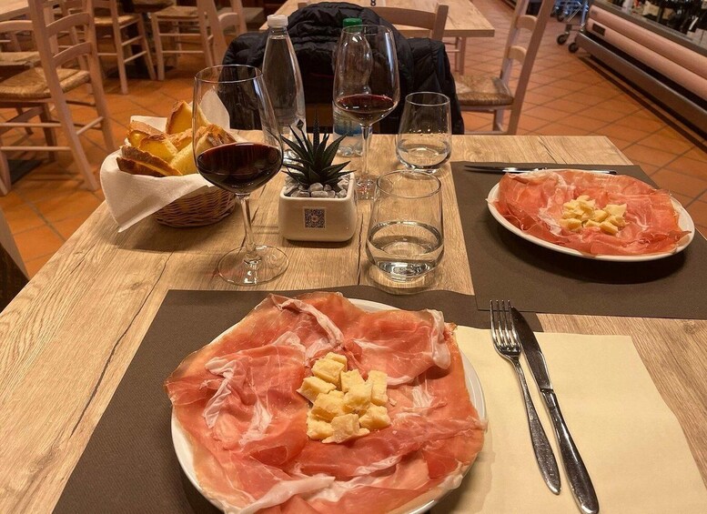 A table with a plate of prosciutto and pineapple, wine glasses, a water bottle, and a small plant. 4