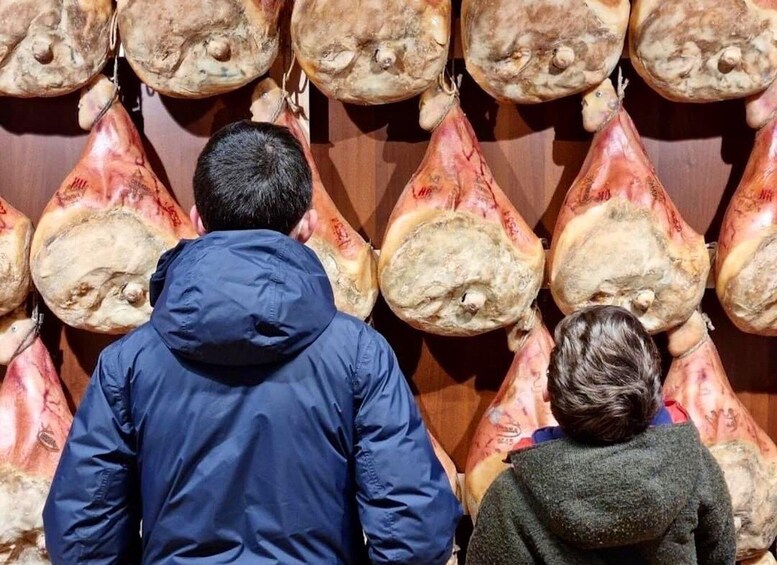 A person in a blue jacket and another in a grey sweater looking at large, irregularly shaped objects hanging from a wall. 1