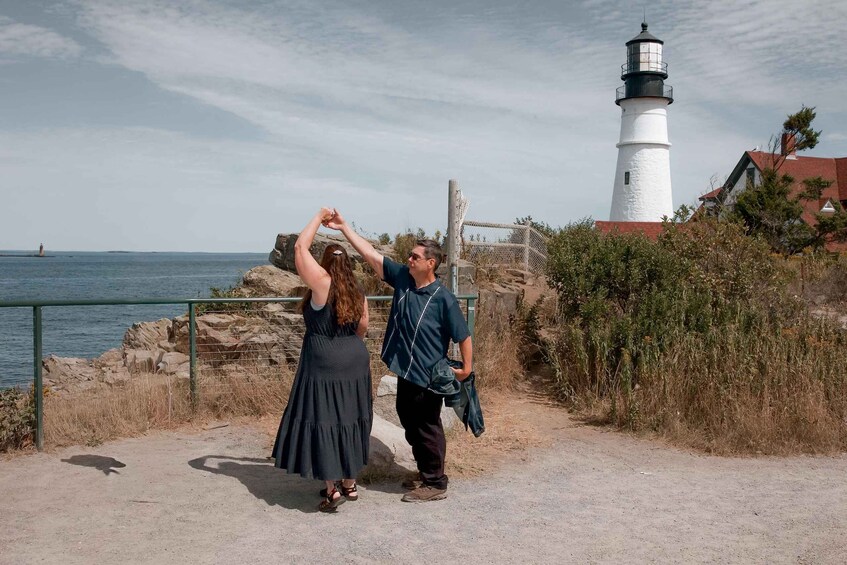 A couple dancing by a rocky shoreline with a lighthouse in the background. 4