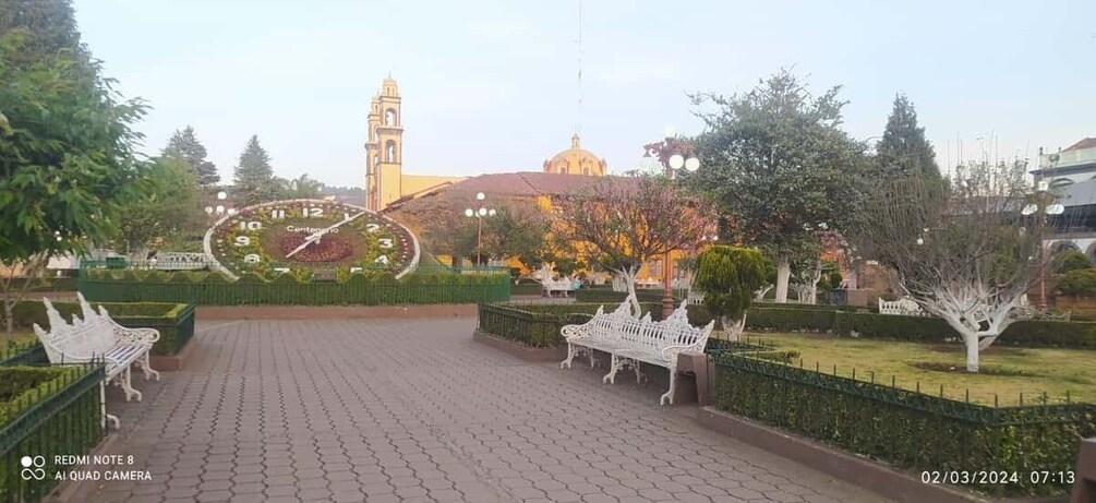 A park with a clock, benches, and a distant bell tower. 4