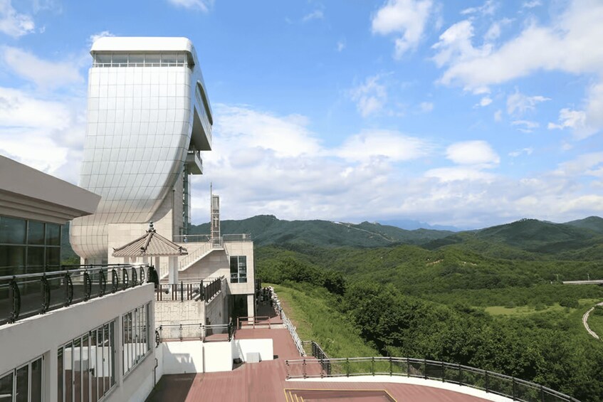 A modern building with a unique curved design, overlooking a lush green valley and distant mountains. 1