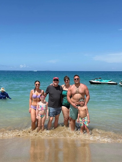 A family of five at a beach with clear blue water and a boat in the background. 3