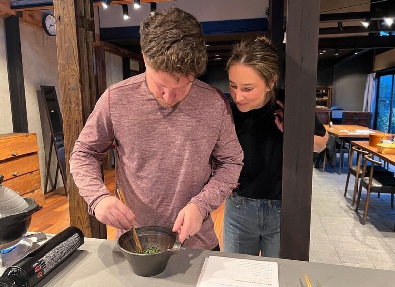 A person cooking with a pot on a stove, another person standing beside them, and a dining area in the background. 3