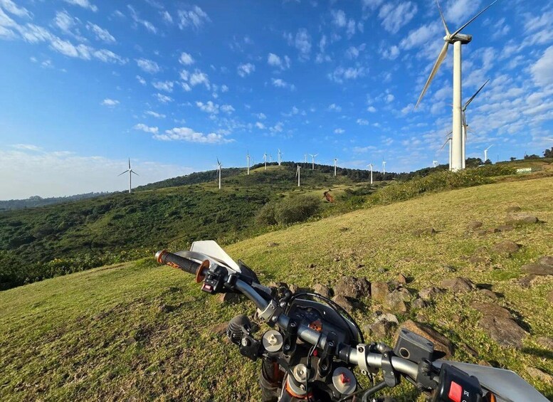 A motorcycle on a grassy hill with wind turbines in the background. 4