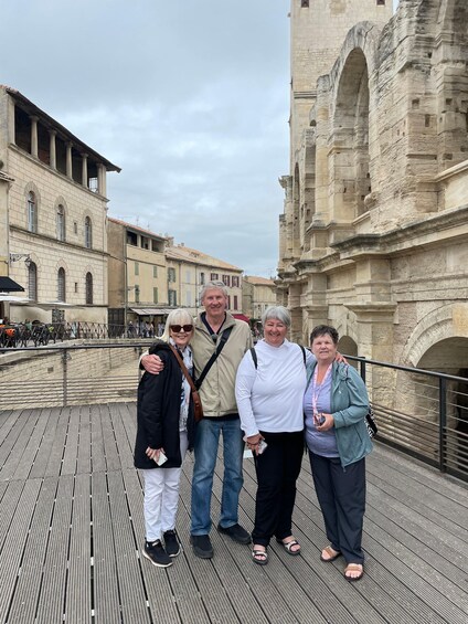 A group of people standing on a wooden bridge with historic buildings in the background. 1