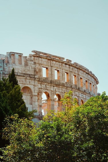 An ancient stone amphitheater with multiple arches and columns, surrounded by lush greenery. 1