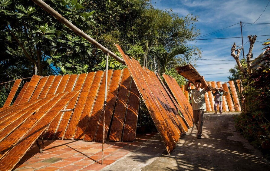 A person carrying a large wooden structure on their head, walking on a dirt path. 4